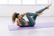 © F8  \ Suport Ukraine - Young fit woman exercising in a gym lying on mat doing leg raising and twisting exercises. Young attractive woman doing abs workout. Fitness woman doing a sit up.