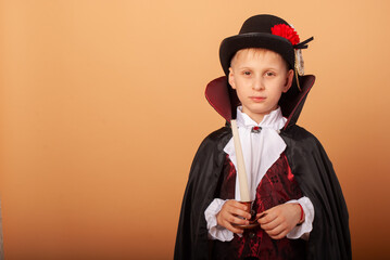 Wall Mural - a child of American appearance with a frightening look isolated on a beige background in the costume of Count Dracula vampire on Halloween