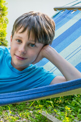 Caucasian boy 8 years old on a hammock in the garden smiling at the photographer