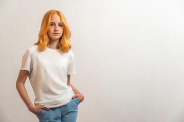 Wall Mural - Portrait of a teenage girl with red hair and a white T-shirt on a light background