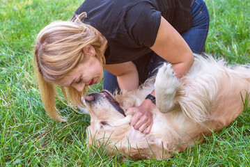 Wall Mural -  girl playing with a dog of breed golden retriever in the park