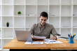 © kamiphotos - Young businessman sitting and checking financial documents displayed in chart format, young businessman who founded a startup company, managing a new business to grow by leaps and bounds.
