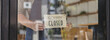Close-up shot of a closed sign in front of a storefront, a café employee standing holding a store opening-closing sign, flipping over a sign that says 