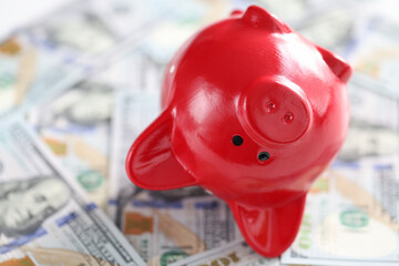 Inverted red piggy bank lies on one hundred dollar bills