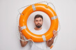 © WHstudio Leushin N - Attentive man lifeguard looks through lifebuoy cares about accident prevention ready to rescue people during emergency situation poses against white background. Young male model learns to swim
