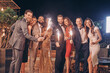 © gstockstudio - Group of beautiful people in formalwear holding sparklers and smiling while spending time on outdoor party