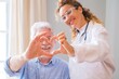© Daniel - Close up of young female doctor and senior man showing heart sign with hand at home. Doctor helping senior patient and giving care. Elderly medical health care.