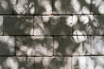 Wall Mural - Textured background of stone wall with shadow from tree outdoors, rough decorative light gray large brick. Structural material for exterior wall decoration
