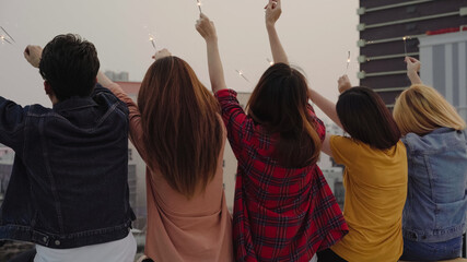 Wall Mural - Outdoor shot of young people at rooftop party. Happy group of asian friends enjoy and play sparkler at roof top party at evening sunset. Holiday celebration festive party. Teenage lifestyle party.