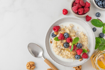 Wall Mural - Healthy breakfast. Quinoa porridge with fresh berries, nuts and mint in a bowl with spoon on white background. top view