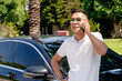© Vladimir Razgulyaev - a young Asian businessman, a man in a white shirt and sunglasses, stands near a modern car and talks on a mobile phone, solves problems and questions, smiles