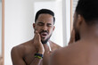 Handsome 30s African guy with frown face expression reflected in mirror touch cheek while brush teeth, feeling pain due oral dental problems. Toothache, sensitive enamel need repair toothpaste concept