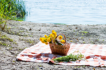 picnic on the beach. Basket with yellow flowers, glasses of wine. Resting time near lakes