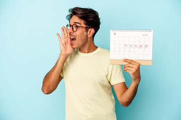 Young mixed race man holding calendar isolated on blue background shouting and holding palm near opened mouth.