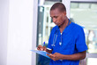© vystekimages - young serious doctor man taking notes on clipboard.