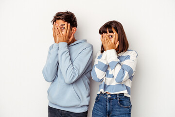 Wall Mural - Young mixed race couple isolated on white background blink through fingers frightened and nervous.