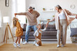 © JenkoAtaman - Active senior grandparents dancing with two happy kids grandchildren in living room