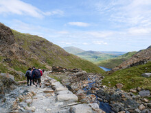 Rear View Of Group Of Distant Hikers With Backpacks Walking Down The Miners' Track From Mount Snowdon In Stunning Scenery Of Mountains In Wales