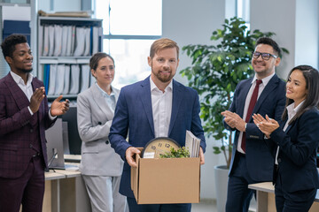 Wall Mural - Group of intercultural colleagues clapping hands to new employee carrying box with supplies