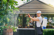 Caucasian male gardener in uniform, protective glasses and gloves spraying flowers at garden with chemicals. Man protecting plants from pests during summer time. 