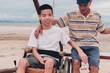 Happy disabled teenager boy smiling face with parent on outdoors activity at the beach, Vacation of people with disabilities and family in nature outside , Mental health concept.