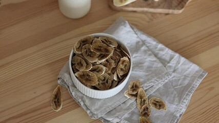 Wall Mural - dried bananas in a white plate. Dehydrated slices of banana chips. A linen napkin, a mug. fresh sliced banana on a board. A healthy food snack.