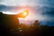 © zakalinka - Silhouette of woman meditating and practicing yoga and rock pebble pyramid on the beach, spiritual mental health practice, meditation, harmony and balance concept