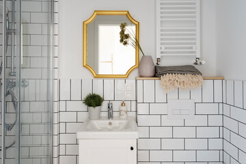 luxurious small bathroom with white design tiles, bathroom sink and stylish gold mirror on the wall.