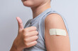 An arm of a boy with adhesive bandage plaster on it after vaccination showing thumb up, injection covid vaccine, healthcare for children and teenagers