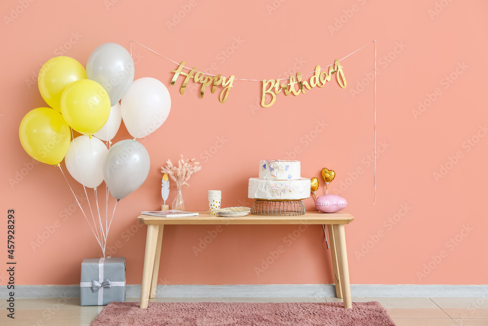 Table with birthday cake and balloons near color wall