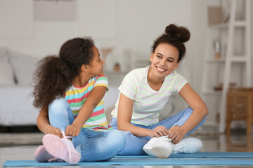 Canvas Print - African-American little girl with her mother tying shoe laces at home