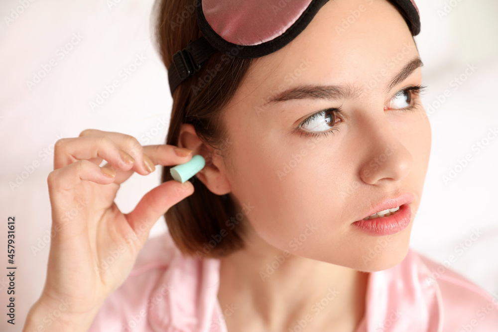 Young woman putting ear plug in bedroom, closeup