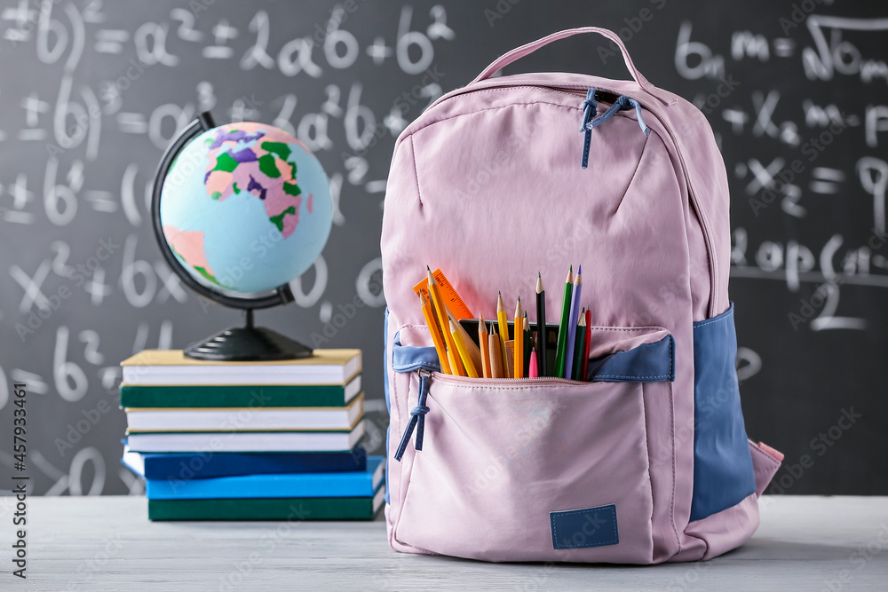 School backpack with stationery, books and globe on table in classroom