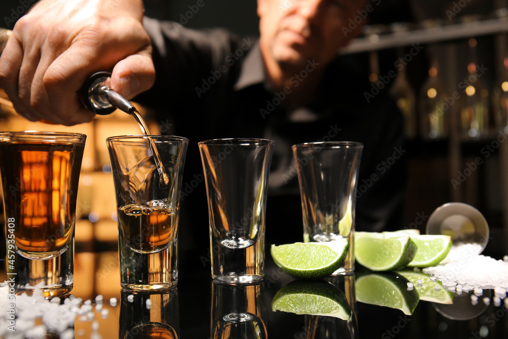 Bartender pouring tasty tequila into glasses at table in bar, closeup