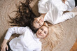 © diignat - Beautiful blonde mother and lovely brunette daughter lying on round carpet