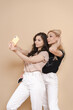 © diignat - Portrait of beautiful blonde mother and her daughter making a selfie using smart phone and smiling, on beige background.