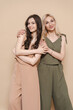 © diignat - Blonde mother and brunette adult daughter wearing identical clothes, different colors, posing over beige background
