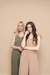 © diignat - Blonde mother and brunette adult daughter wearing identical clothes, different colors, posing over beige background