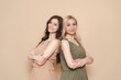 © diignat - Blonde mother and brunette adult daughter wearing identical clothes, different colors, posing over beige background