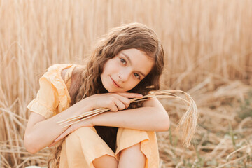 Beautiful teenage girl with long hair walking through a wheat field on a sunny day. Outdoors portrait. Schoolgirl relaxing