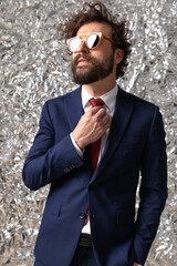 Poster - cool sexy businessman fixing his tie, wearing sunglasses