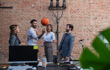 Wall Mural - Group of cheerful young businesspeople playing basketball in office, taking a break.