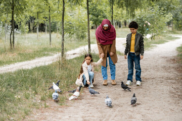 Wall Mural - Arabian mother and kid standing near birds in park