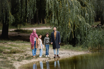 Wall Mural - Arabian family smiling at camera near lake in park