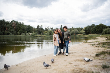 Sticker - Happy muslim man hugging kids near birds and lake during autumn