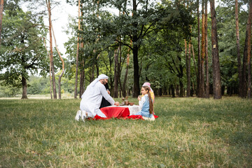 Poster - Positive arabian father sitting near family during picnic in park