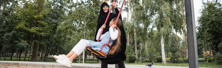 Poster - Arabian woman playing with daughter on swing outdoors, banner