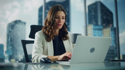 Wall Mural - Portrait of Successful Young Businesswoman Sitting at Her Desk Working on Laptop Computer in Big City Office. Professional Social Media Strategy Manager Plan Disruptive e-Commerce Campaign