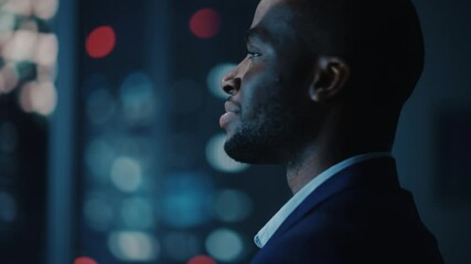 Wall Mural - Night Office: Proud Close-up Portrait of Powerful Black Businessman Wearing Suit Standing, Looking out of the Window on a Big City. Ambitious African CEO Thinking of e-Commerce Investment Strategy