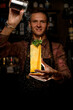 © fesenko - hand of bartender gently holds glass of cocktail with drinking straws and mint and sprinkling on it with sugar powder